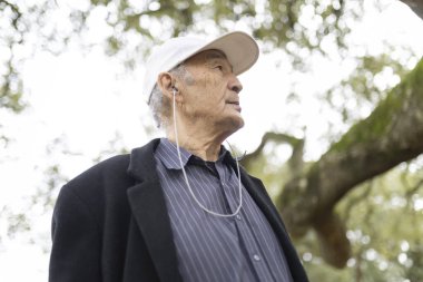 Yaşlı adam parkta müziği seviyor, eğlence ve teknolojiyi kucaklıyor.