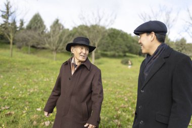 Baba ve oğul birlikte güzel vakit geçiriyorlar, sakin bir sonbahar parkında sakin bir yürüyüş ve sohbetin tadını çıkarıyorlar.