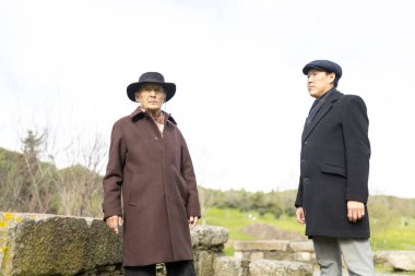 İki arkeolog bulutlu bir günde eski harabeleri keşfediyor, kışlık palto ve şapkalar giyiyorlar.