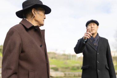 Asyalı turist rehberi, arkeoloji parkına yaptığı bir ziyarette, üst düzey bir adama işitme cihazı takan bir adama bir şey anlatıyor.