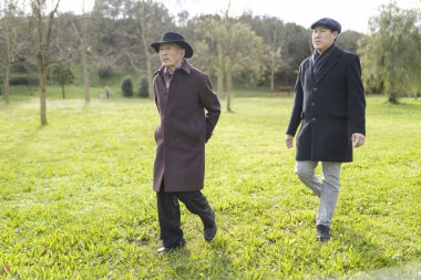 Yaşlı bir baba ve yetişkin bir oğul, aile bağlarını ve nesillerarası bağları temsil eden bir parkta keyifli bir gezinti yapıyorlar.