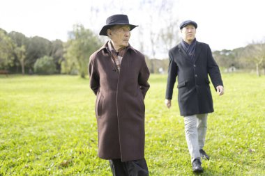 İki yaşlı Asyalı adam güneşli bir günde parkta keyifli bir gezinti yapıyorlar.