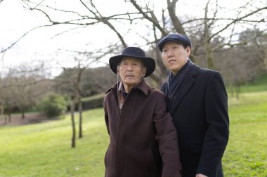 Yetişkin oğlu, parkta birlikte vakit geçirip aile bağlarının ve nesiller arası ilişkilerin önemini gösteren yaşlı babasına destek oluyor.