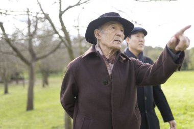 Kıdemli çiftçi, meyve bahçesindeki genç meslektaşına işaret edip anlatıyor.