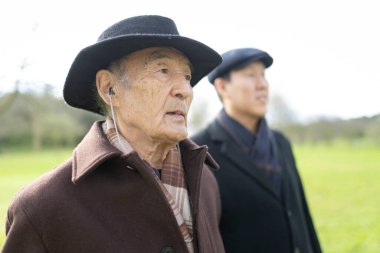 Yaşlı Asyalı şapkalı ve kulaklıklı bir adam oğluyla parkta yürümekten hoşlanıyor.