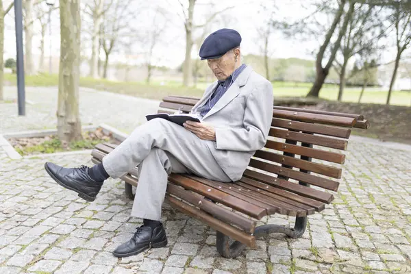 Kulaklık takan kıdemli bir adam parkta bankta otururken defterine not alıyor.