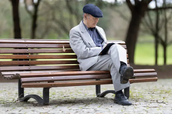 Yaşlı profesör bir bankta otururken defterine not alıyor.