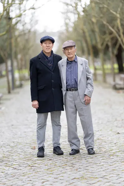 Yetişkin oğlu, parkta birlikte yürürken, aile bağlarını ve bakıcılıklarını gösteren yaşlı babasına destek oluyor.