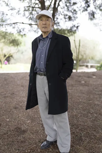 Beyzbol şapkası ve uzun bir palto giyen, parkta poz veren şık bir son sınıf öğrencisinin portresi.