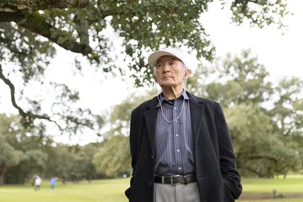 Şapka takan ve kulaklık takan yaşlı bir adam parkta müzik dinliyor.