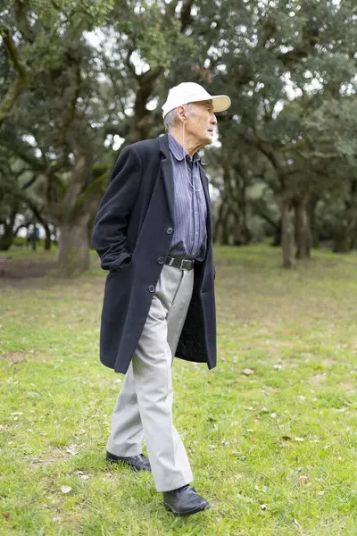 Yeşil bir parkta rahatlatıcı bir yürüyüş sırasında müziğin keyfini çıkaran yaşlı bir adam sağlıklı ve aktif bir yaşam tarzı sergiliyor.