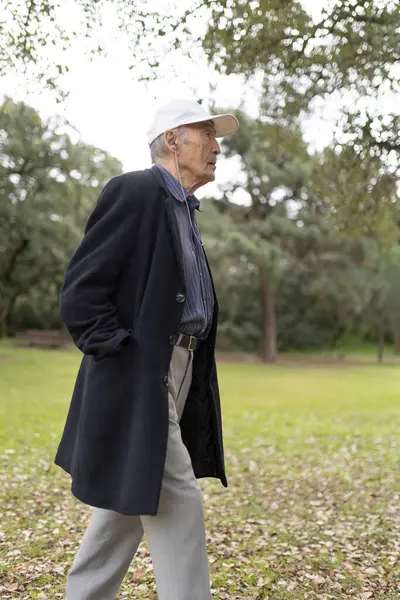 Paltolu ve şapkalı yaşlı bir adam huzurlu bir parkta rahatça geziniyor.