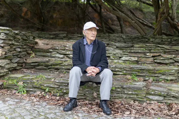 Kıdemli adam, doğayla çevrili bir parkta taş basamaklarda otururken huzur dolu bir anın tadını çıkarıyor.