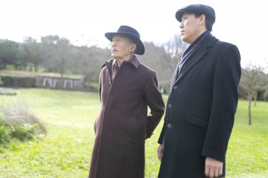 Şapkalı yaşlı bir adam ve parktaki sohbetin tadını çıkaran daha genç bir adam.