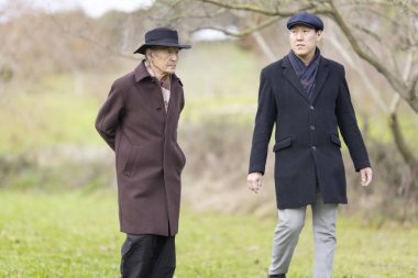 Yaşlı adam ve iş adamı parkta birlikte yürüyor, sohbetin ve temiz havanın tadını çıkarıyorlar.