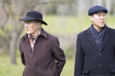 Paltolu, şapkalı ve eşarplı iki kıdemli Asyalı parkta yürüyorlar.