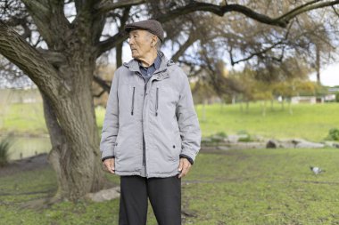 Kulaklıklı yaşlı adam yeşil bir parktaki bir ağacın altında müzik dinleyerek huzur buluyor.