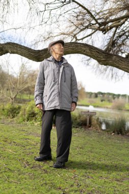 Yaşlı bir adam gölün yakınındaki bir parkta duruyor, doğada huzurlu bir anın tadını çıkarıyor.