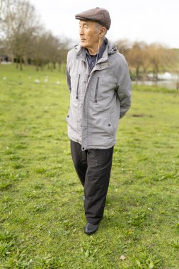 Yaşlı bir adam bulutlu bir günde çimenli bir parkta yürüyor.