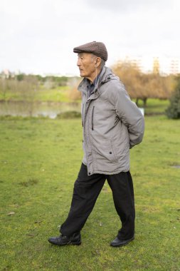 Kıdemli Asyalı adam yeşil bir parkta rahatça dolaşırken müzik dinliyor.