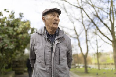 Yaşlı Asyalı adam parkta yürürken kulaklıkla müzik dinliyor.