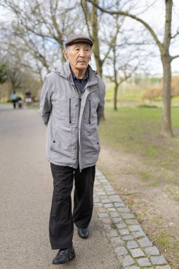 Kıdemli Asyalı adam huzurlu bir parkta rahatça geziniyor, temiz havanın ve sükunetin tadını çıkarıyor.