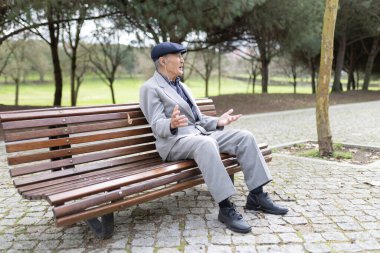 Yaşlı işadamı kulaklık takıyor, parkta bankta oturuyor, müzik dinliyor ve konuşuyor.