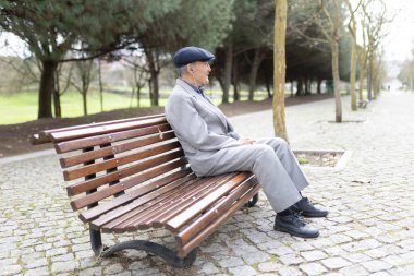 Huzurlu bir parkta bankta otururken kulaklıkla müzik dinlemeyi seven kıdemli bir adam.