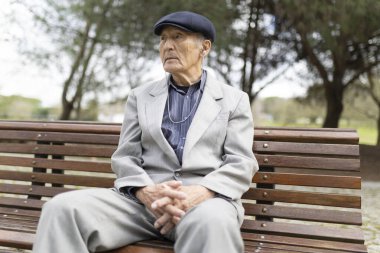 Takım elbiseli, düz şapkalı, kulaklıklı bir adam parkta bankta otururken müziğin keyfini çıkarıyor.