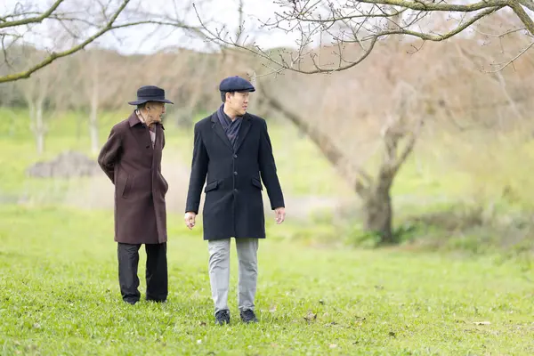Yetişkin oğlu kışın parkta kıdemli babasıyla yürüyüp konuşur.