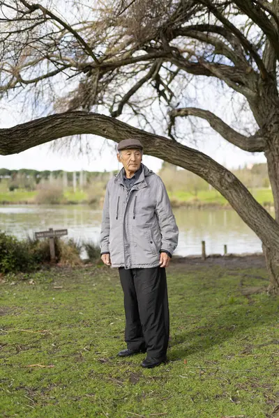 Huzurlu bir parkta gölün kenarında duran yaşlı adam, doğanın huzurunun tadını çıkarıyor.