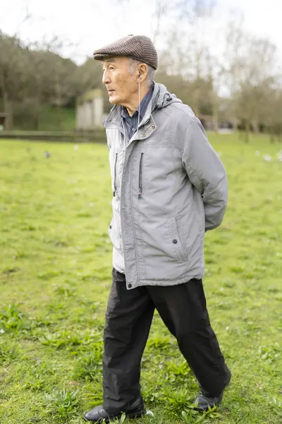 Yaşlı bir adam yeşil bir parkta rahatlatıcı bir yürüyüş sırasında müziğin keyfini çıkarıyor.