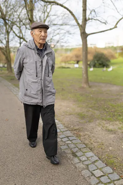 Huzurlu bir parkta huzur içinde yürüyüp emekliliğinin tadını çıkaran yaşlı bir adam.