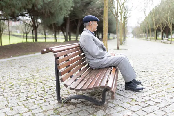 Huzurlu bir parkta bankta otururken kulaklık takan beyefendi müzik dinliyor.