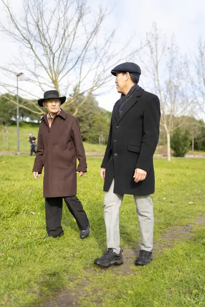 İki iyi giyimli son sınıf öğrencisi parkta yürürken sohbet etmekten zevk alıyor.