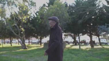 Son sınıf öğrencisi ceketli ve şapkalı huzurlu bir parkta geziniyor.