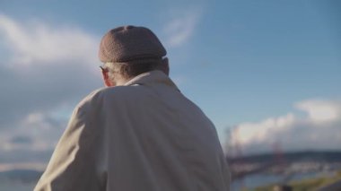 Kulaklık takan son sınıf öğrencisi şehir manzarasına tepeden bakan bir parkta müzik dinliyor.