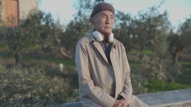 Kulaklık takan yaşlı bir adam parkta bankta oturuyor.
