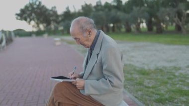 Park bankında otururken dijital tablet üzerinde resim çizen odaklanmış son sınıf öğrencisi.