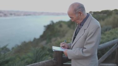 Kıdemli adam deniz kenarındaki defterine not alıyor.