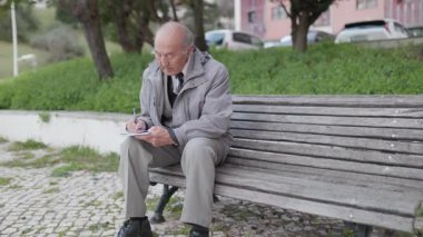 Kıdemli adam bir bankta otururken defterine not alıyor.