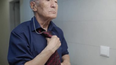 Kıdemli adam güne hazırlanıyor, işitme cihazı takıyor ve kravatını düzeltiyor.