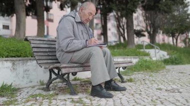 Kıdemli adam notlar alıyor sessiz bir parkta bankta oturuyor.