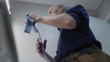 Kıdemli adam mavi kravatı katlarken kulaklıkla müzik dinliyor.