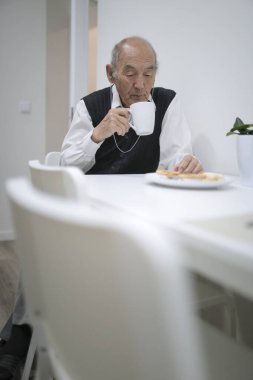 Kıdemli adam, modern, parlak evinde çay ve kurabiyelerle sakin bir anın tadını çıkarıyor.