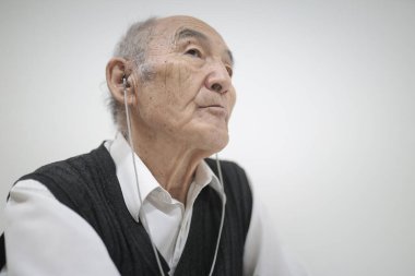 Yaşlı adam kulaklık kullanıyor, teknolojiyi kucaklıyor ve müzik veya ses içeriğinden zevk alıyor