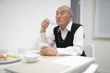 Yaşlı adam evde kahvaltı yapıyor, işitme cihazı kullanıyor.