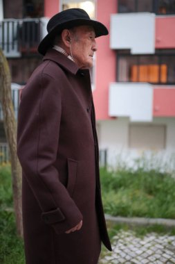 Dışarıda müzik dinleyen, şapka ve kulaklık takan yaşlı bir adam.