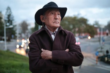 Son sınıf öğrencisi kulaklıklarla müzik dinlerken loş bir şehir ortamında dalgın dalgın uzaklığa bakıyor.