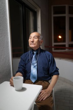 Yaşlı profesör gömlek ve kravat takıyor, geceleri balkonunda kahvenin tadını çıkarıyor.